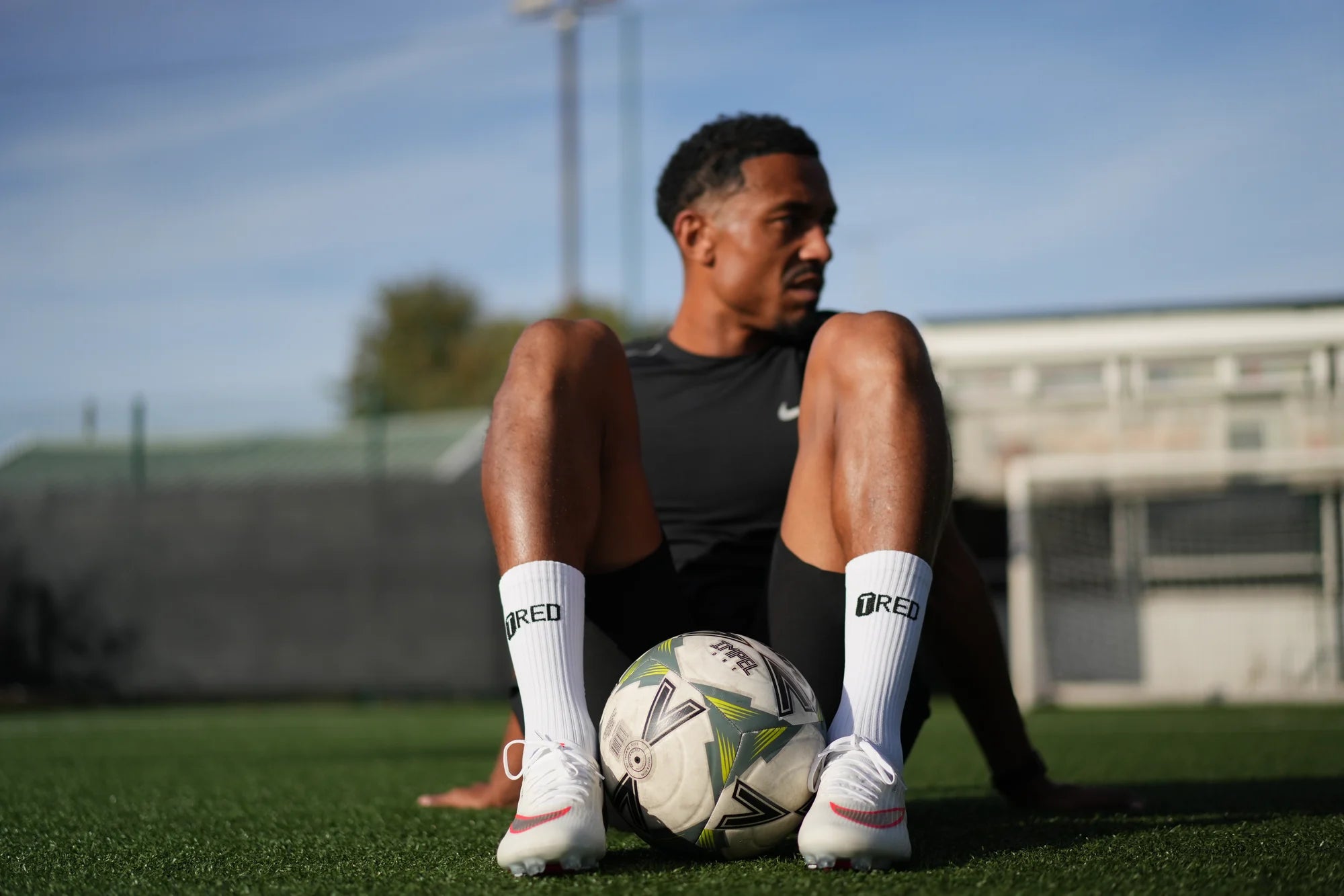 Player sitting on the pitch with a ball, wearing TRED socks